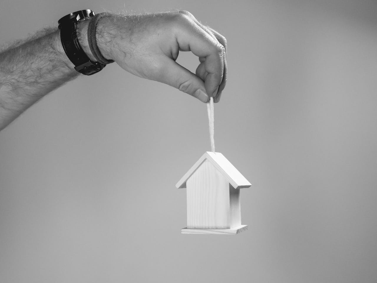 A hand holding a wooden house toy house from string